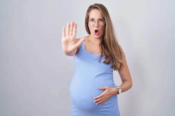 若いです妊娠中の女性は白い背景の上に立っています手でジェスチャーを停止します 怒りとフラストレーション式 — ストック写真