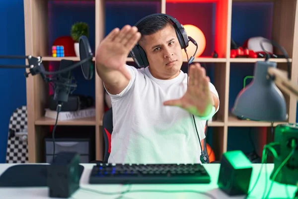 Young hispanic man playing video games doing frame using hands palms and fingers, camera perspective