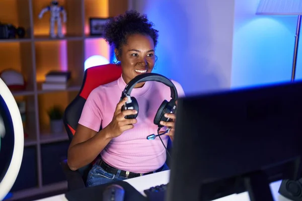 アフリカ系アメリカ人女性ストリーマー笑顔自信を持って保持ヘッドフォンでゲームルーム — ストック写真