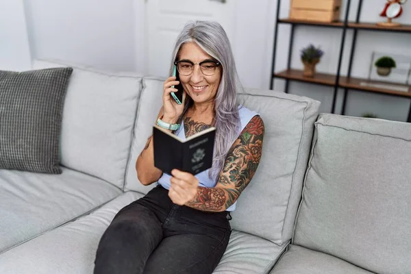 Middle age grey-haired woman talking on the smartphone holding passport at home