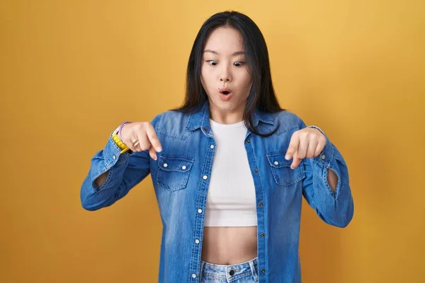 Молодая Азиатка Стоит Жёлтом Фоне Указывая Пальцами Рекламу Удивлённое Лицо — стоковое фото