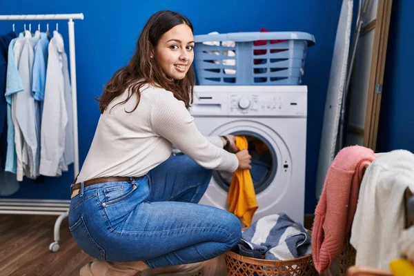 若い美しいヒスパニック系の女性が洗濯室で自信を持って洗濯服を笑顔 — ストック写真