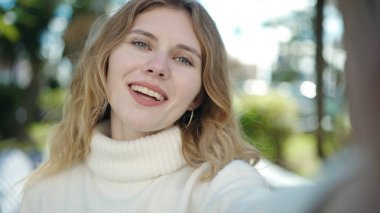 Young blonde woman smiling confident making selfie by camera at park