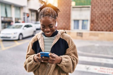 Afro-Amerikalı kadın sokakta akıllı telefon kullanarak kendine güveniyor.