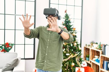 VR gözlük takan genç İspanyol adam Noel ağacının yanında duruyor.