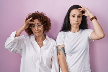 İspanyol anne ve kızı pembe arka plan üzerine gündelik beyaz tişört giyiyorlar. Alnındaki sorun yüzünden endişeli ve stresli. Kriz için endişeli. 