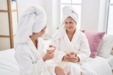 Mother and daughter wearing bathrobe drinking coffee at bedroom