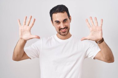 Beyaz arka planda duran yakışıklı İspanyol adam on numarayı gösterip işaret ederken kendinden emin ve mutlu gülümsüyor.. 