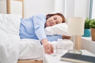 Senior woman lying on bed holding pills at bedroom