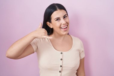 Pembe arka planda durup gülümseyen, el ve parmaklarıyla telefonla konuşan İspanyol bir kadın. iletişim kavramları. 