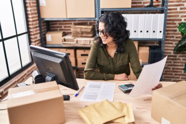 Genç Latin kadın ecommerce iş işçisi ofiste belge okuyor.