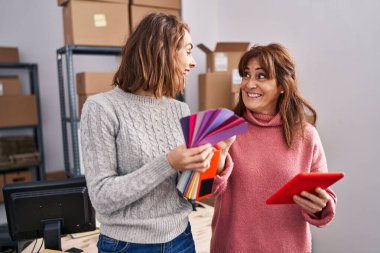 Two women ecommerce business workers using touchpad choosing color at office