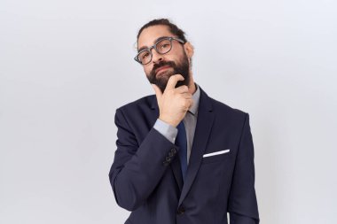 Sakallı, takım elbiseli ve kravatlı İspanyol bir adam kameraya kollarını kavuşturup gülümseyerek ve çenesini kaldırarak bakıyor. Olumlu düşünmek. 