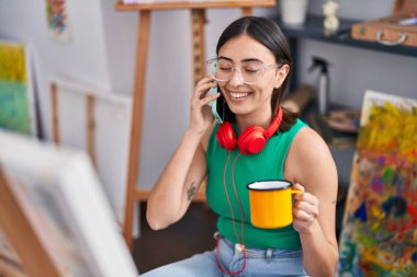 Genç İspanyol kadın sanatçı akıllı telefonla konuşuyor. Sanat stüdyosunda kahve içiyor.