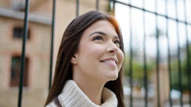 Young beautiful hispanic woman smiling confident looking to the sky at street