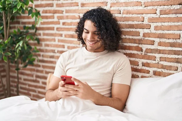 Kıvırcık Saçlı Akıllı Telefon Kullanan Spanyol Bir Adam Yatakta Otururken — Stok fotoğraf