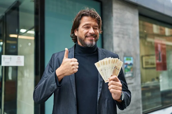 百デンマーククローネ紙幣を保持ハンサムな中年男性笑顔と正 親指アップ優れたと承認サインを行う — ストック写真