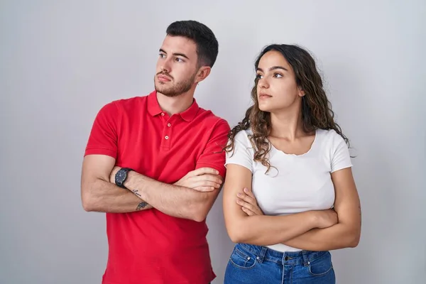 Young Hispanic Couple Standing Isolated Background Looking Side Arms Crossed — Stock Photo, Image