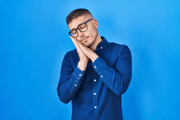 Jonge Spaanse Man Draagt Bril Blauwe Achtergrond Slapend Moe Dromend — Stockfoto