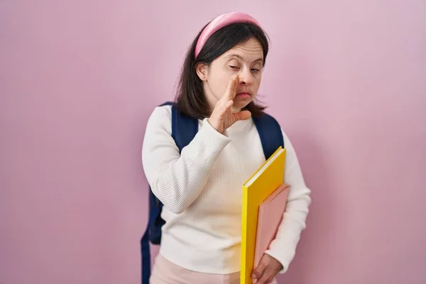 ダウン症候群の女性は学生のバックパックを着て 本を手で口に秘密噂を伝えます 悪意のある話の会話をささやく — ストック写真