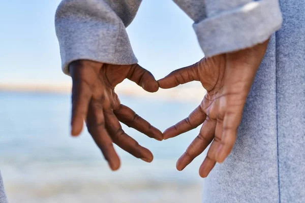Man and woman couple doing heart gesture with hands at seaside