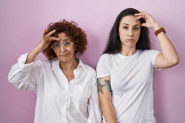 ヒスパニック系の母親と娘を身に着けていますカジュアルな白いTシャツ上ピンクの背景心配し 額に手で問題について強調 神経と危機への不安 — ストック写真