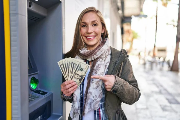 Young Blonde Woman Holding Dollars Banknotes Atm Machine Smiling Happy — стоковое фото