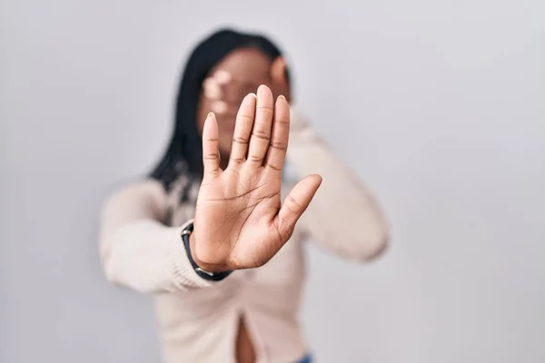 African woman with braids standing over white background covering eyes with hands and doing stop gesture with sad and fear expression. embarrassed and negative concept.
