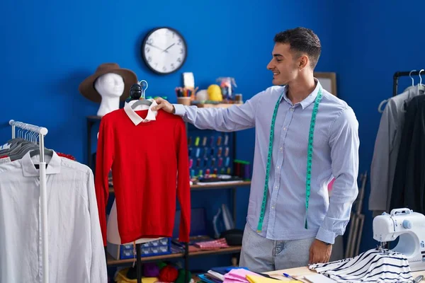 Joven Hombre Hispano Sastre Sonriendo Confiado Sosteniendo Camiseta Estudio Costura —  Fotos de Stock