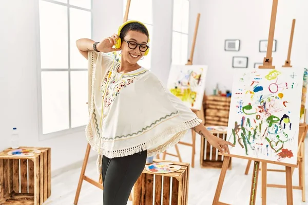 Genç İspanyol kadın sanat stüdyosunda müzik dinlerken kendinden emin bir şekilde gülümsüyor.