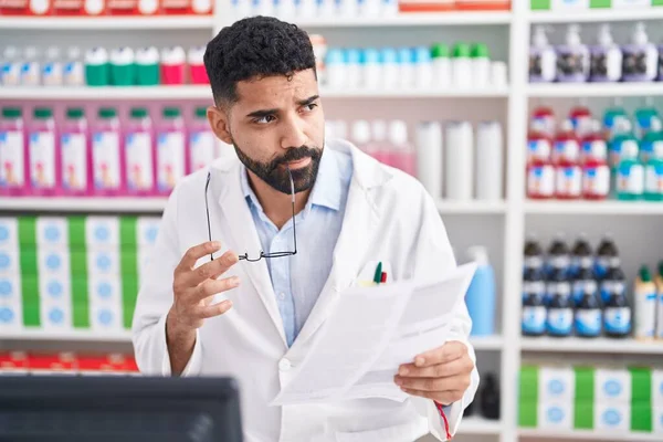 Young Arab Man Pharmacist Reading Document Doubt Expression Pharmacy — Zdjęcie stockowe