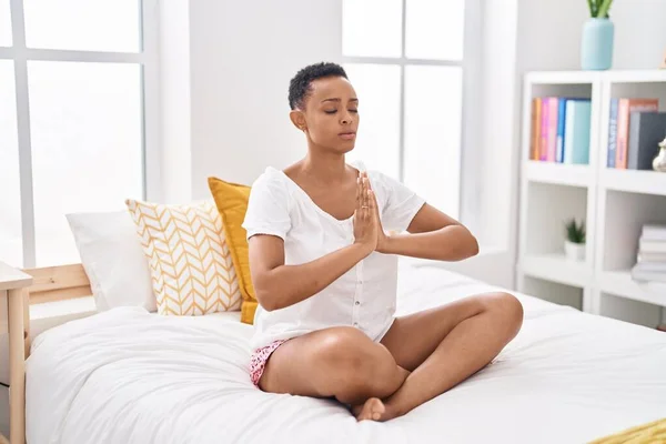 African american woman doing yoga exercise sitting on bed at bedroom