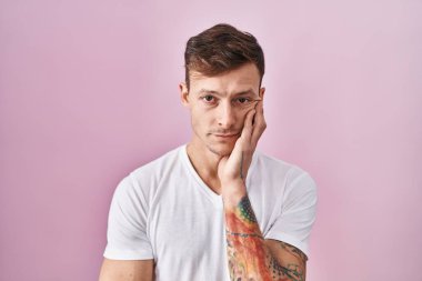 Pembe arka planda duran beyaz bir adam kollarını kavuşturarak depresyondan sıkılmış ve yorgun göründüğünü düşünüyor.. 