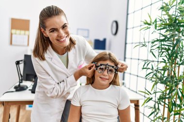 Woman and girl oculist and patient examining vision using optometrist glasses at clinic