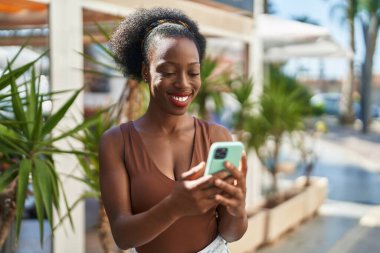 Afro-Amerikalı kadın sokakta akıllı telefon kullanarak kendine güveniyor.