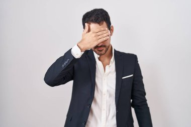 Beyaz arka planda duran yakışıklı İspanyol bir adam. Gülümsüyor ve gülümsüyor. Gözleri şaşkınlıkla örtüyor. kör kavram. 