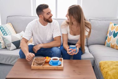 Man and woman couple having breakfast sitting on sofa at home