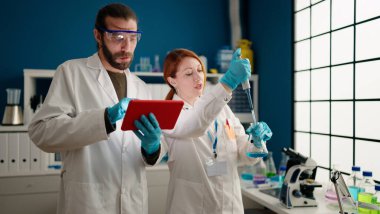 Laboratuvarda dokunmatik ped kullanan bilim adamı ve kadın üniforması giyiyor.