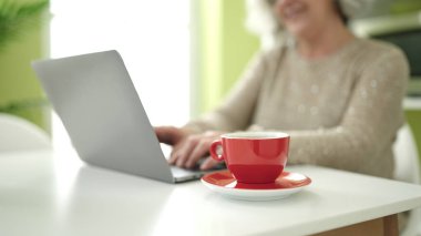 Middle age woman with grey hair using laptop sitting on table at home