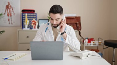 Genç Arap doktor bilgisayarını kullanarak klinikte telefonla konuşuyor.