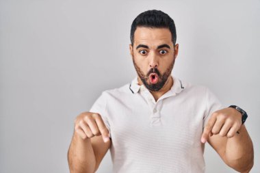 Young hispanic man with beard wearing casual clothes over white background pointing down with fingers showing advertisement, surprised face and open mouth 