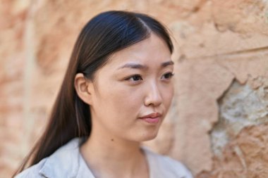 Çinli kadın sokakta rahat bir ifadeyle yan tarafa bakıyor.