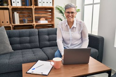 Orta yaşlı kadın psikolog, pischoloji merkezindeki koltukta oturuyor.