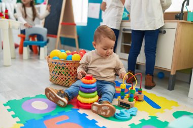 Adorable blond toddler playing with hoops toy sitting on floor at kindergarten