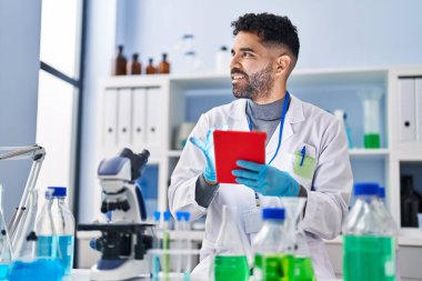 Laboratuvarda dokunmatik ped kullanan genç bir İspanyol bilim adamı üniforması giyiyor.