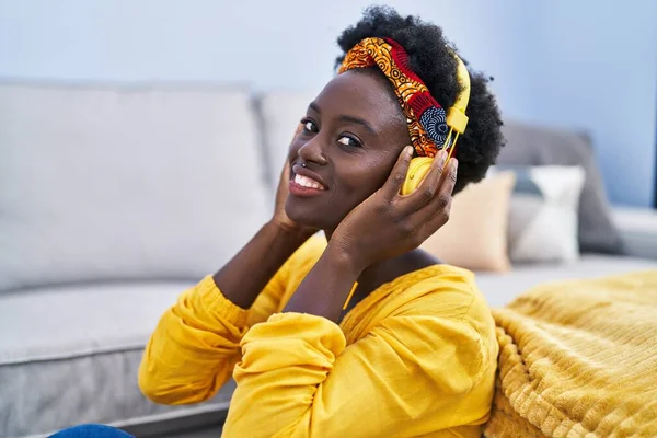 听音乐的年轻非洲裔美国妇女坐在家里的地板上 — 图库照片
