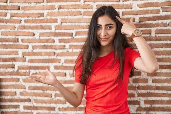 レンガの壁の上に立っている若い10代の少女は混乱し コピースペースを示し 額に指を指すヤシに悩まされました 考えてみてください — ストック写真