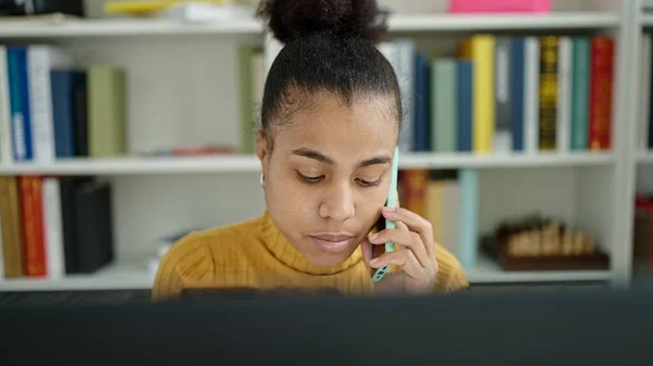 図書館で電話で話すコンピュータを使ってアフリカ系アメリカ人の若い女性の学生 — ストック写真