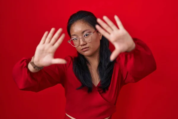 Asian young woman standing over red background doing frame using hands palms and fingers, camera perspective