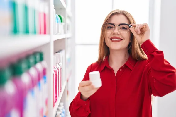 红头发的年轻女性顾客在药店里拿着药瓶 — 图库照片